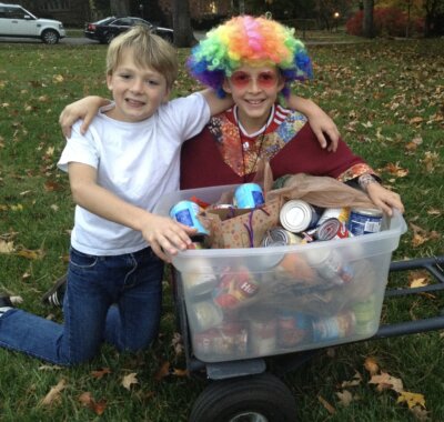 Friends in Halloween costumes lock arms over a box of canned goods they collected on Halloween to Scare Hunger in their community